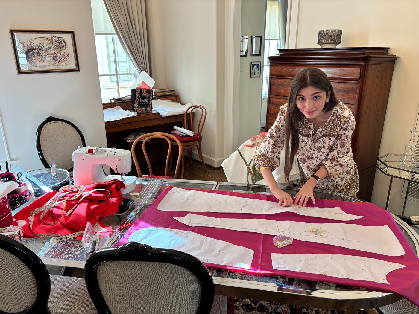 Arta pinning a pink dress pattern across a glass table